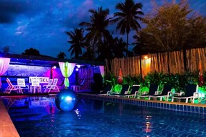 A pool area with lounge chairs and a stage with draped curtains. - Phanganist Hostel (Ko Pha-ngan)
