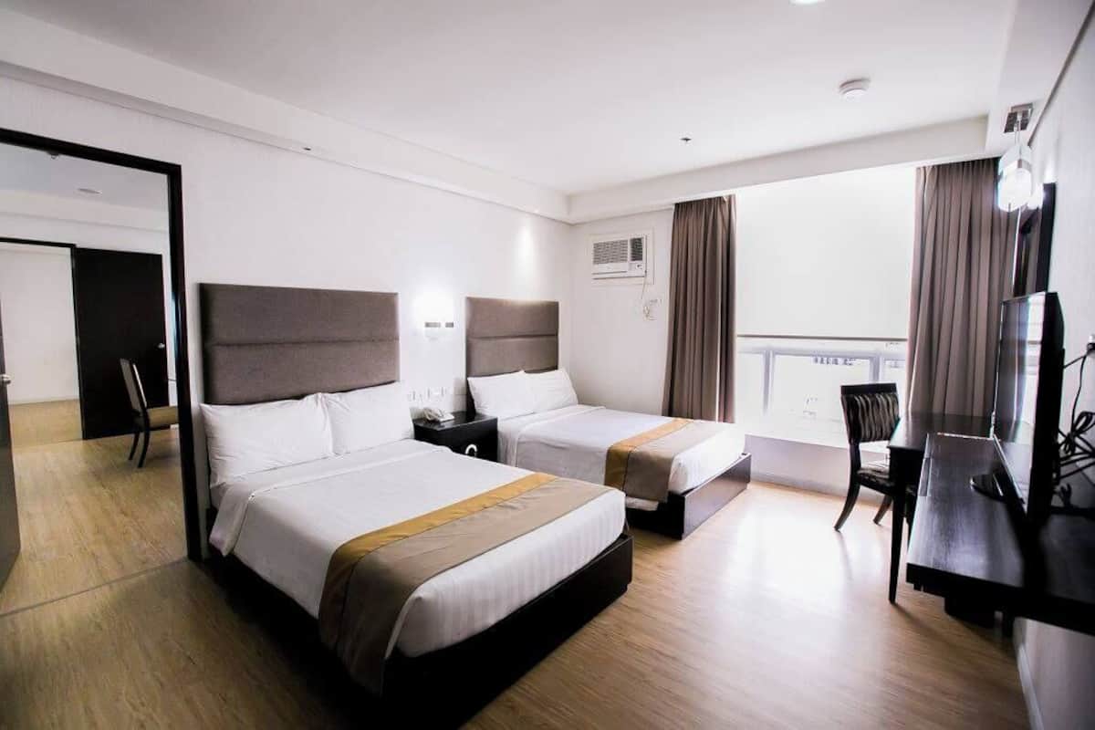 A hotel room with two beds, a desk, a chair, and a TV.