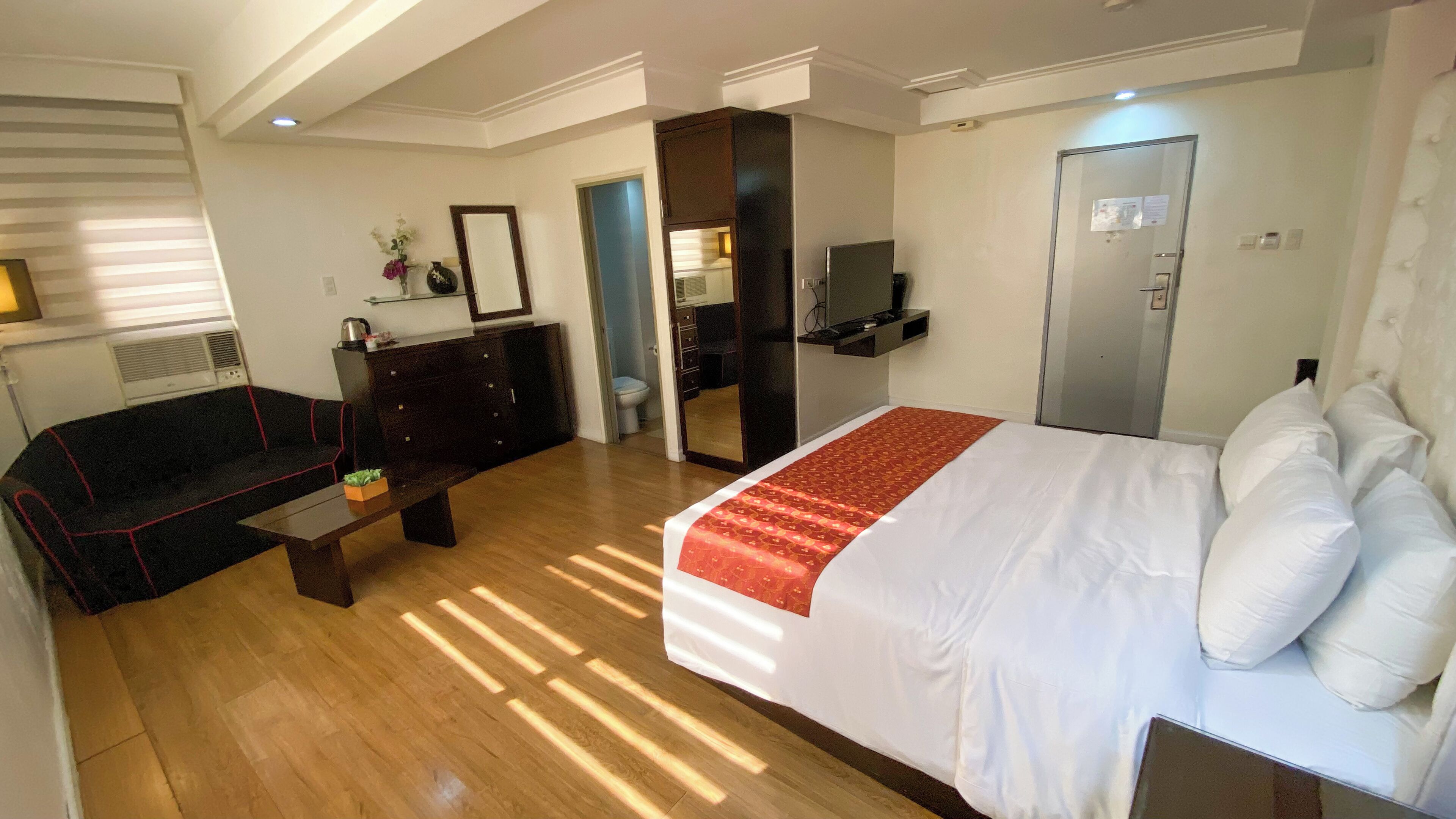 Hotelkamer met een bed, een bureau, een bank, een spiegel, een kledingkast en een badkamer zichtbaar door een open deur.