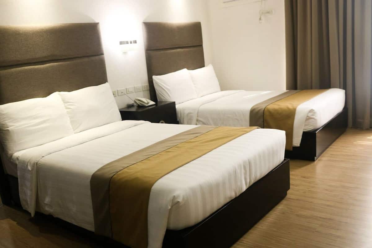Two beds with headboards, a bedside table with a phone, and a wall-mounted light.