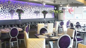 Un restaurante con mesas redondas y sillas moradas, decorado con jarrones de flores.