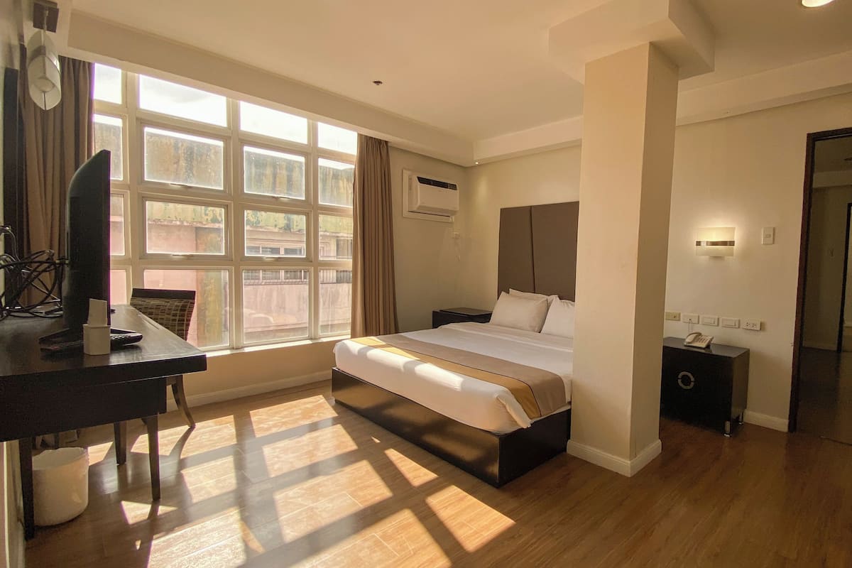 A hotel room with a large bed, a desk with a computer, and a window with curtains.
