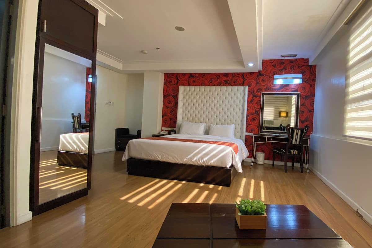 A hotel room with a large bed, a desk with a chair, a mirror, and a window with blinds.