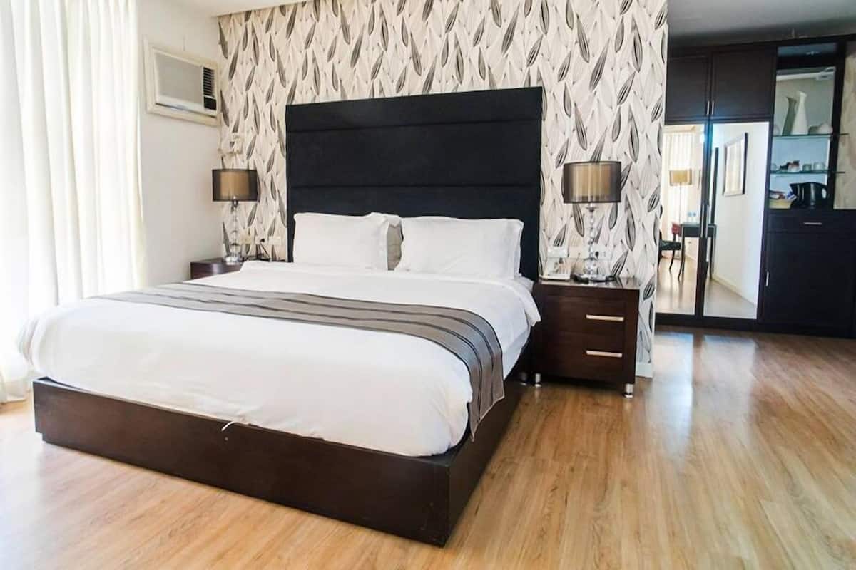 A modern hotel room with a large bed, two bedside tables, and a wardrobe.