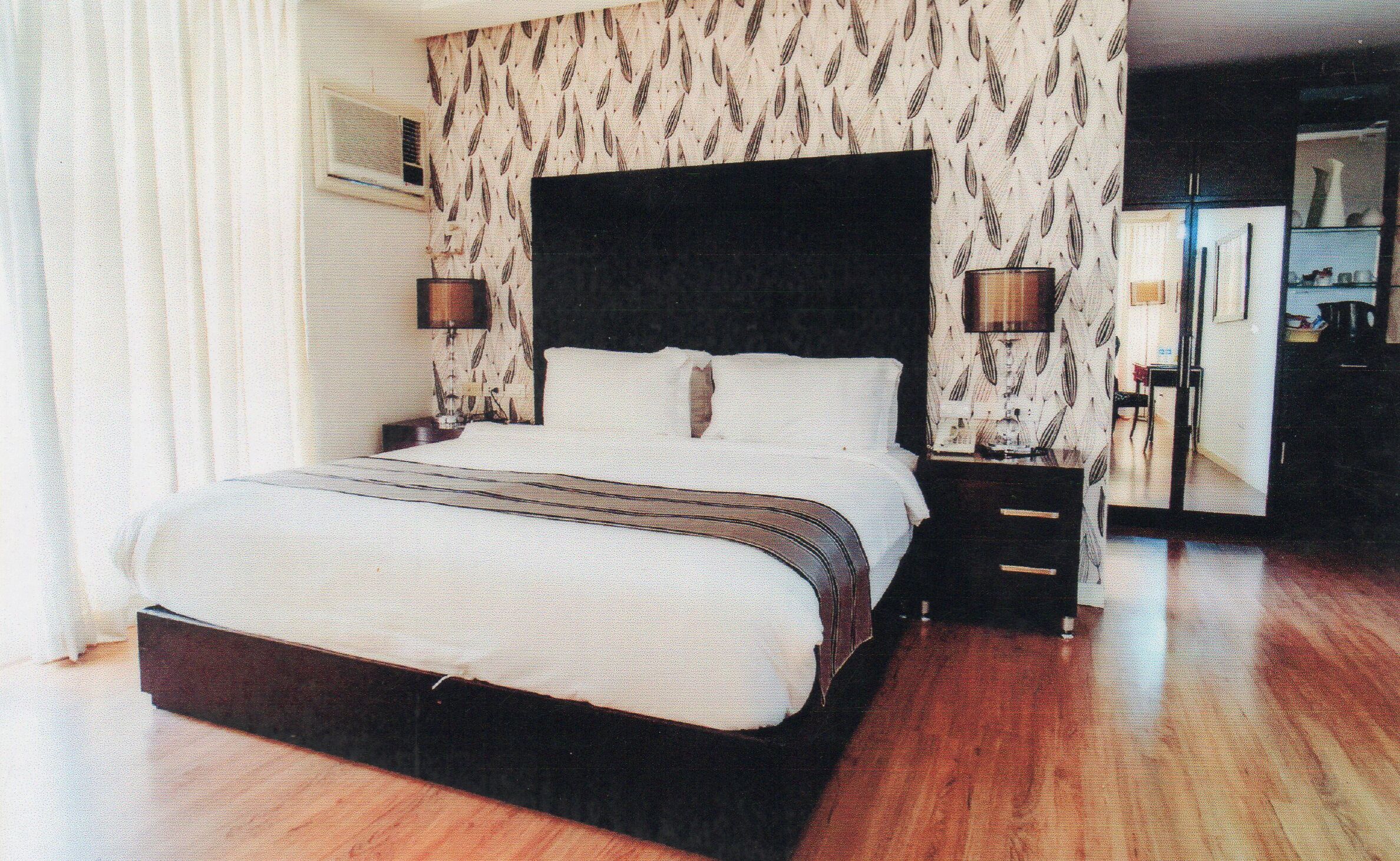 A hotel bedroom with a large bed, two bedside tables, a wardrobe, and a mirror.