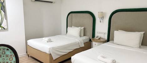 A hotel room with two beds, a bedside table with a phone, and an air conditioning unit on the wall.