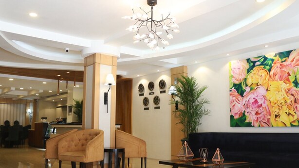 Un vestíbulo con una lámpara de araña moderna, un cuadro floral grande, un mostrador de recepción y una zona de estar con un sofá y sillones.