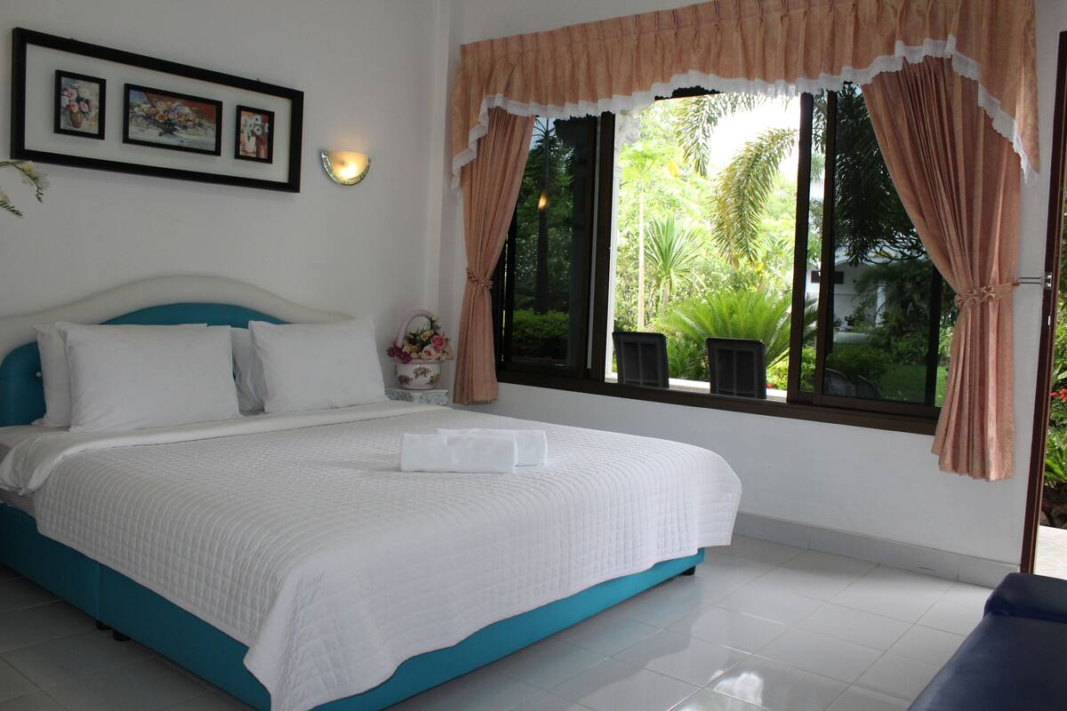 A bedroom with a bed, a nightstand, a window with curtains, and framed pictures on the wall.