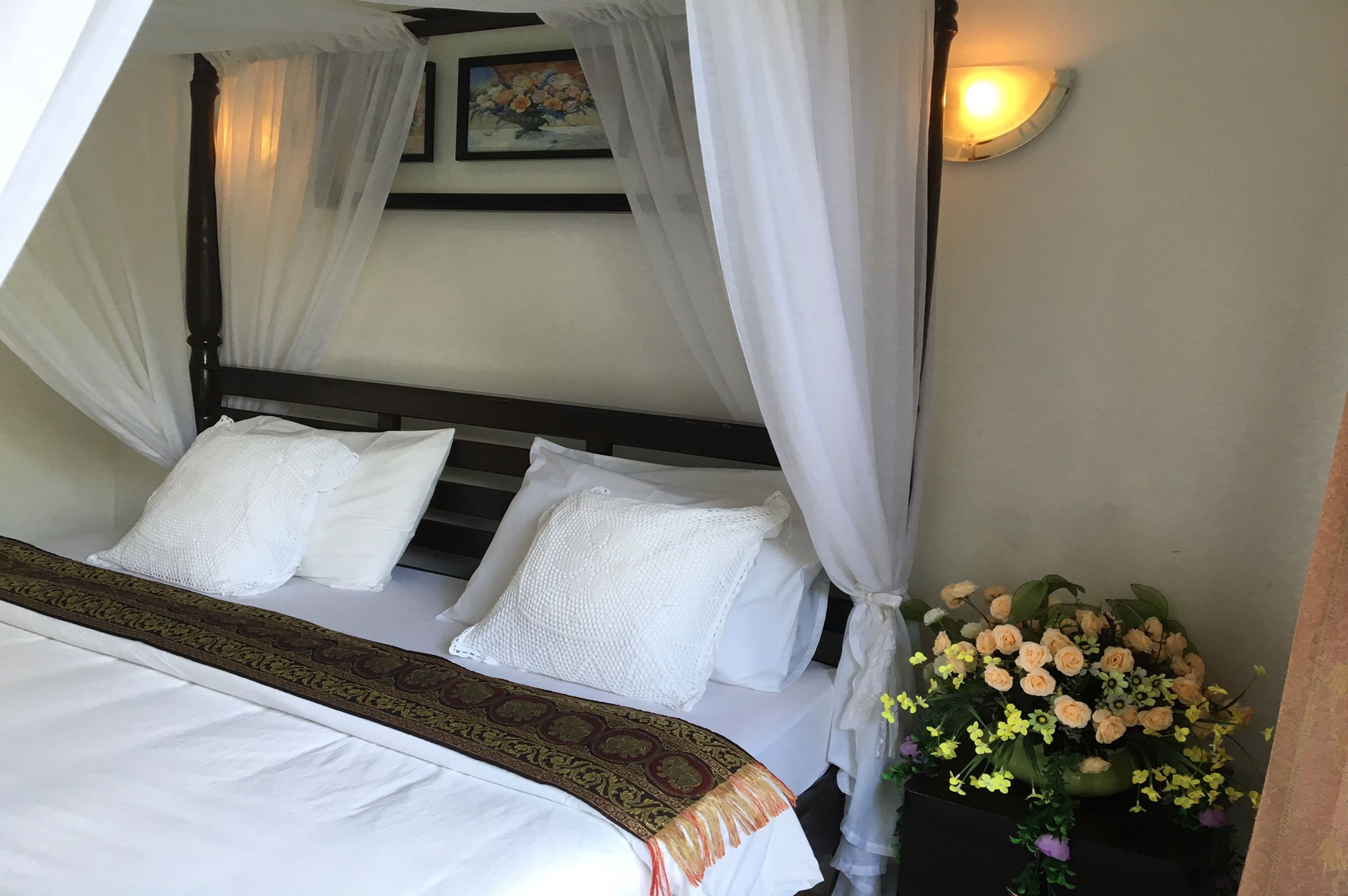 A bed with white linens, a canopy, and a decorative pillow.