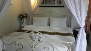 A bed with white bedding and a decorative headboard, a vase with flowers, and a wall with framed pictures.