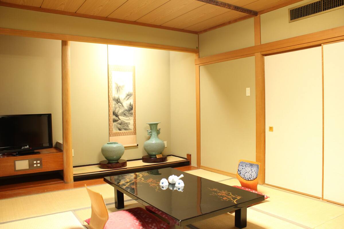 A traditional Japanese room with tatami flooring, a low table, a television, and a sliding door.