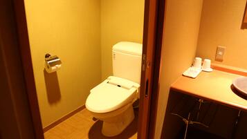 A small, compact bathroom with a toilet, a sink, and a toilet paper holder.