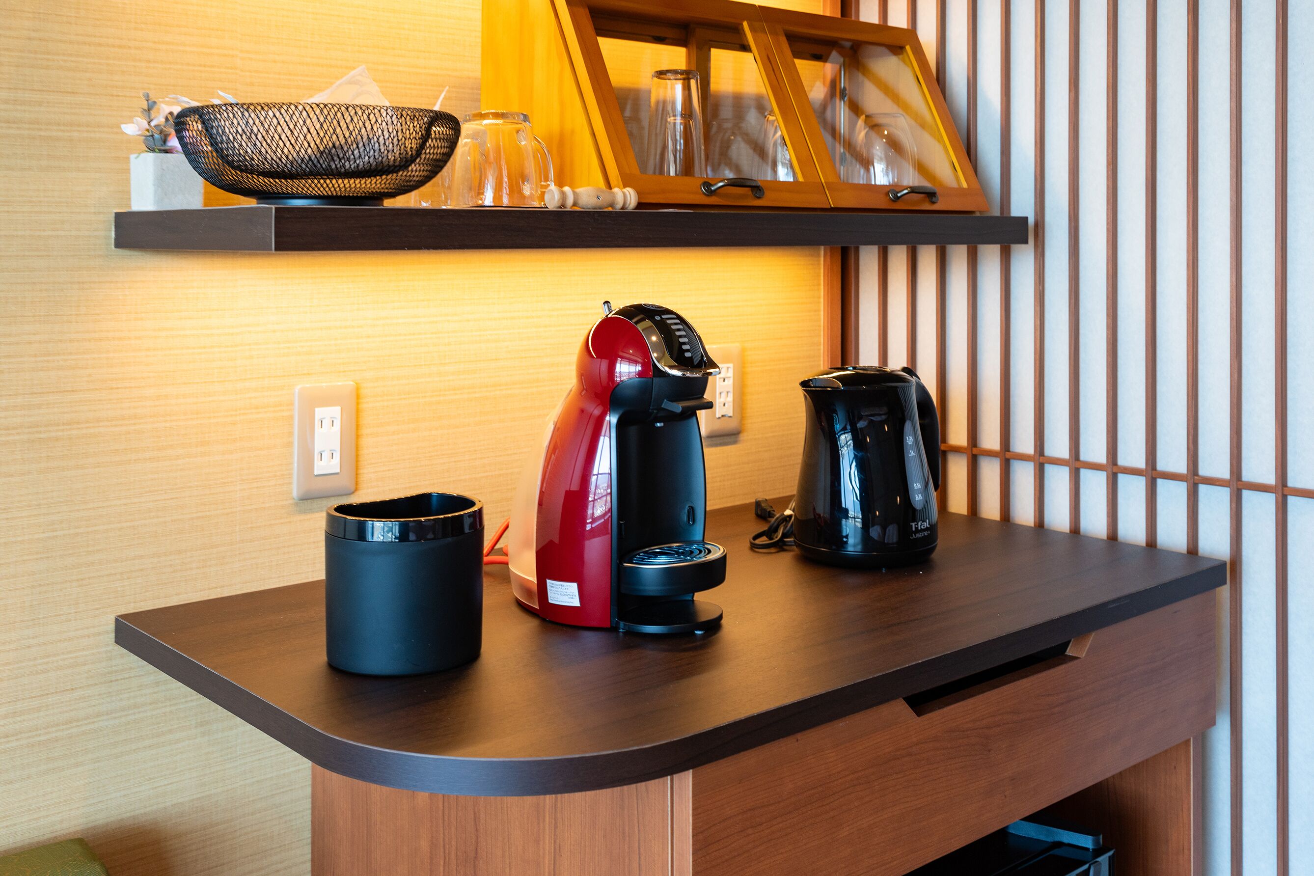 A kitchen counter with a coffee maker, a kettle, and a basket on a shelf above.