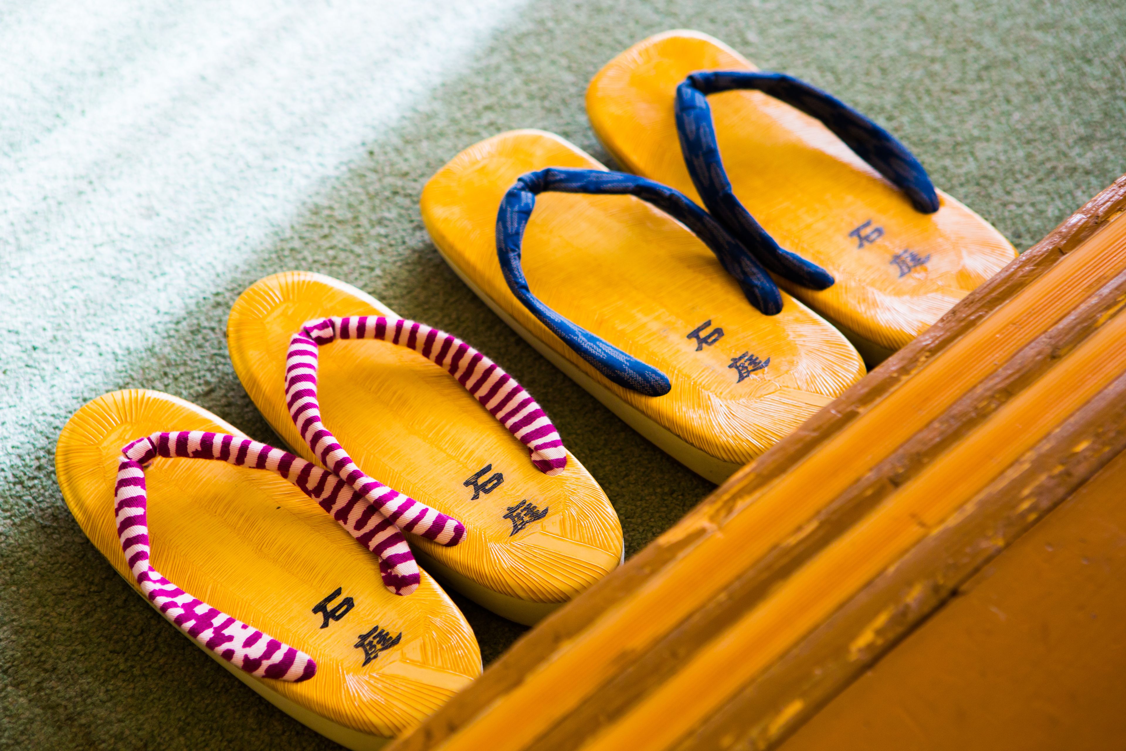 A pair of yellow flip-flops with blue straps and pink trim, placed on a textured surface.