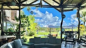 A covered outdoor seating area with wicker furniture, a glass-top coffee table, and a view of a pool and garden. - Palau Central Hotel (Koror)