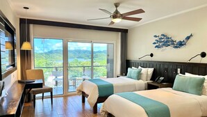 A hotel room with two beds, a desk, a chair, a balcony with a view of the landscape, and a ceiling fan. - Palau Central Hotel (Koror)