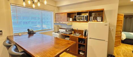 Een kleine keuken met een houten tafel, stoelen, een fornuis, magnetron en een koelkast.