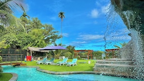 A swimming pool with lounge chairs, a water fountain, and tropical vegetation. - Palau Central Hotel (Koror)