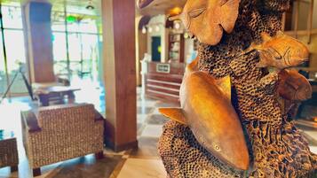 A lobby with a large wooden sculpture of a fish and a tree trunk. There are wicker chairs and a checkered floor.