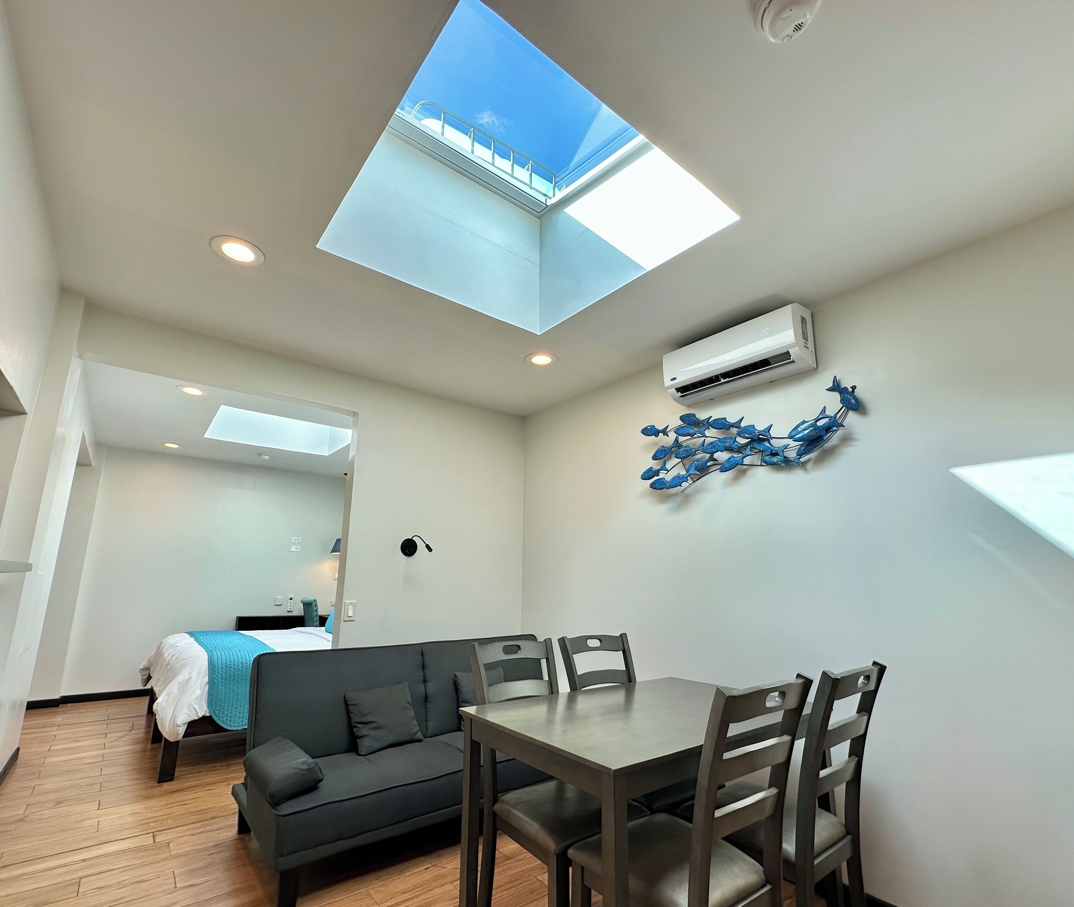Una habitación moderna con tragaluz, una mesa de comedor con sillas, un sofá y un adorno en la pared.
