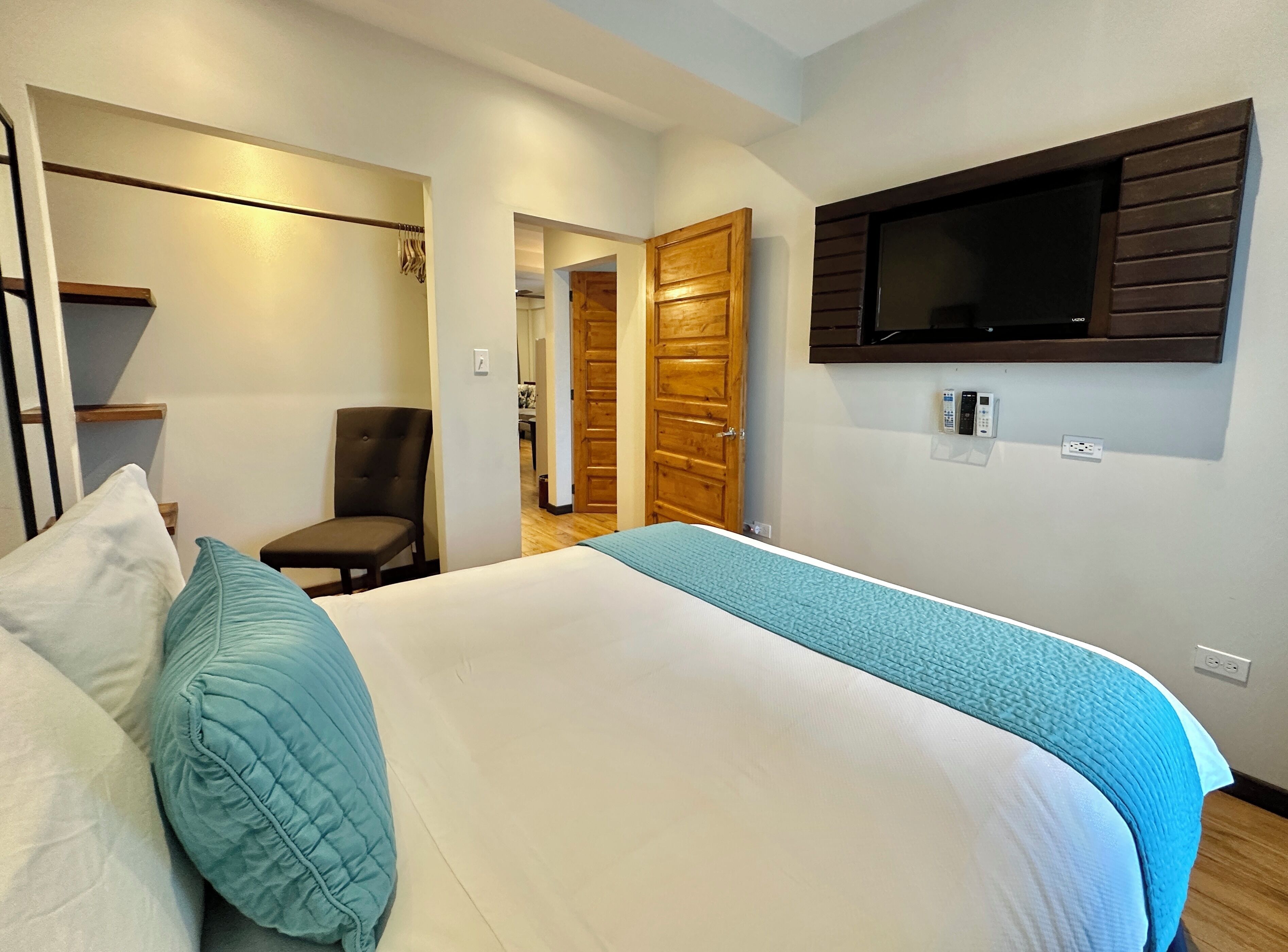 A hotel room with a bed, a chair, a TV mounted on the wall, and a wooden door.