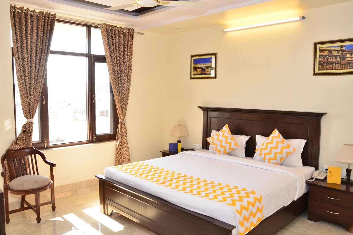 A hotel room with a large bed, a wooden chair, a nightstand, and a window with curtains.