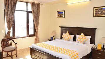 A hotel room with a large bed, a wooden chair, a nightstand, and a window with curtains.