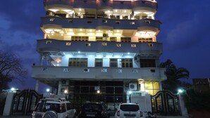 Un edificio de varios pisos con balcones, una entrada con portón y coches aparcados.