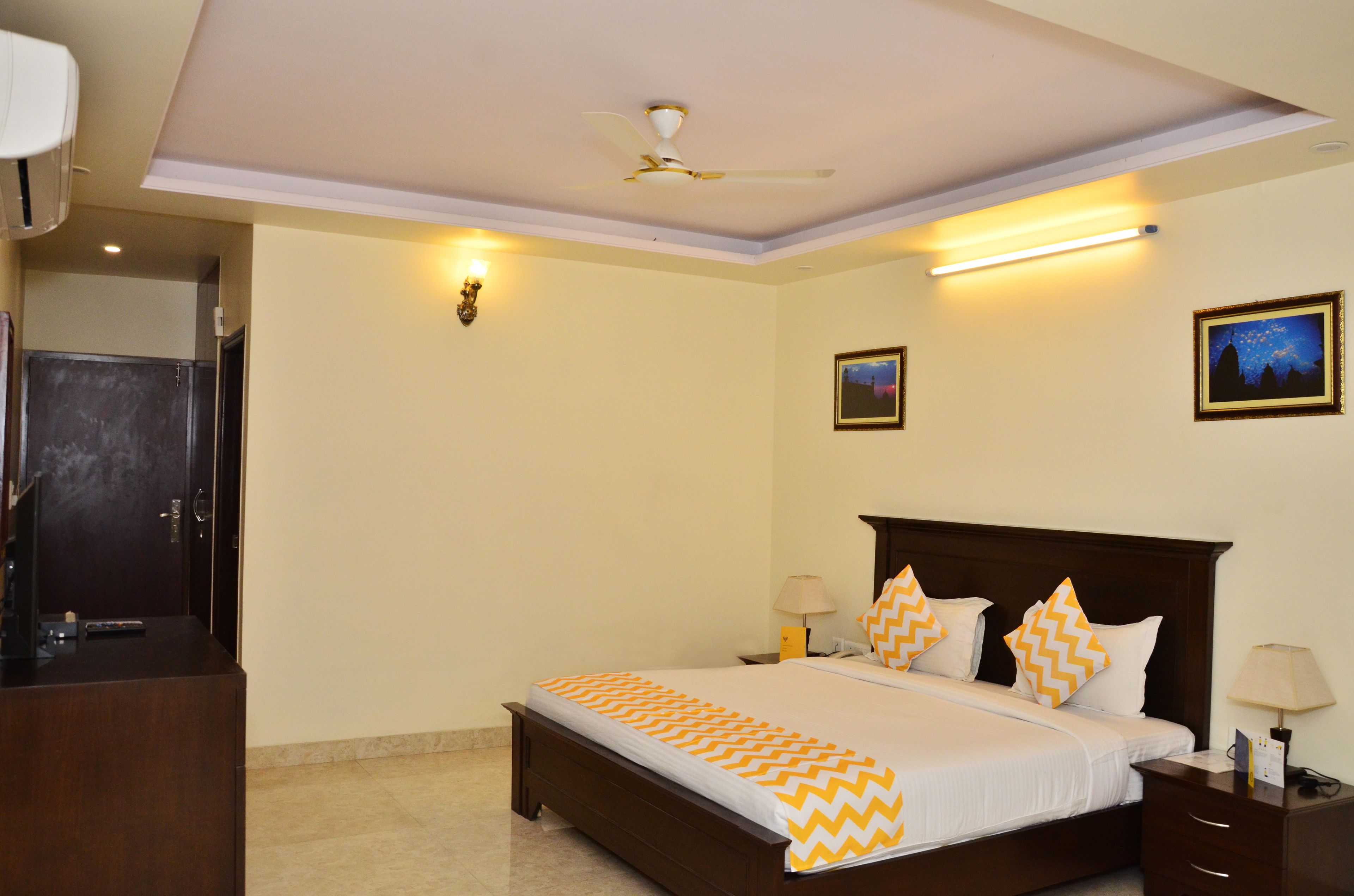Quarto de hotel bem arrumado, com cama, mesas de cabeceira, ventoinha no teto e iluminação embutida na parede.