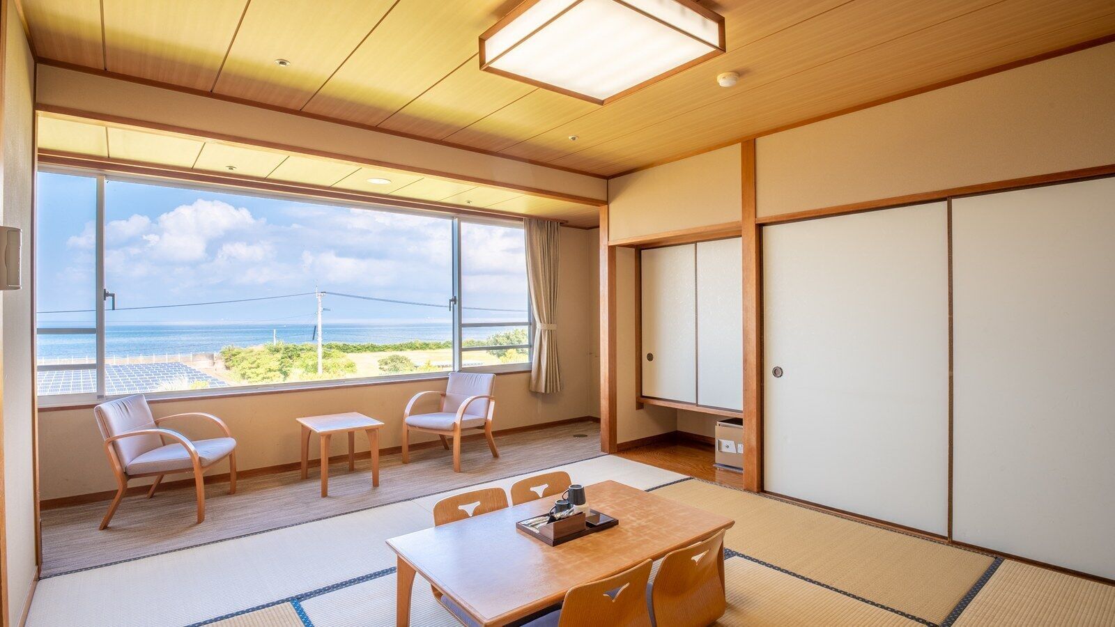 Una habitación japonesa tradicional con suelo de tatami, una mesa baja, sillas, una puerta corredera y vistas al mar.