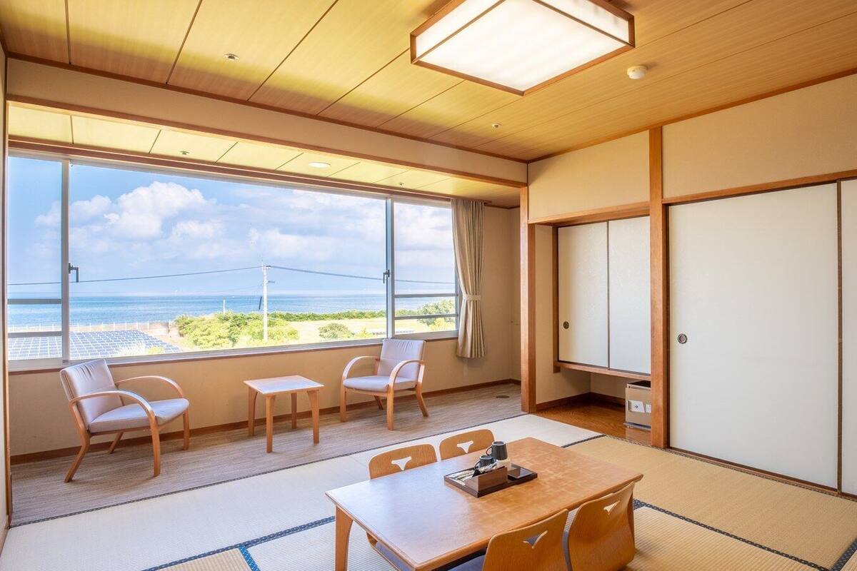 Een traditionele Japanse kamer met tatami vloeren, een lage tafel, stoelen, een schuifdeur en uitzicht op zee.