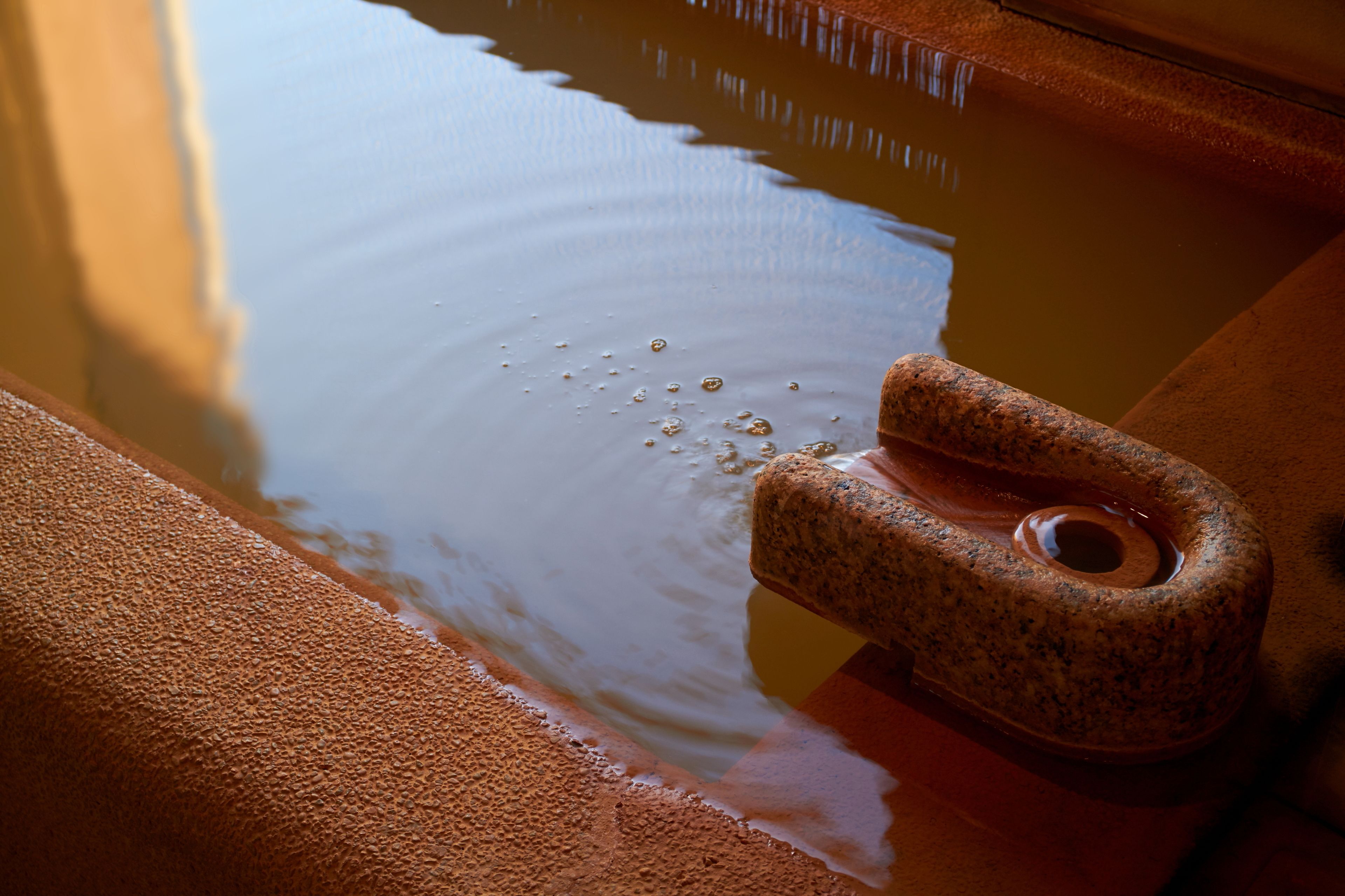A close-up of a stone basin with water and bubbles, reflecting light.