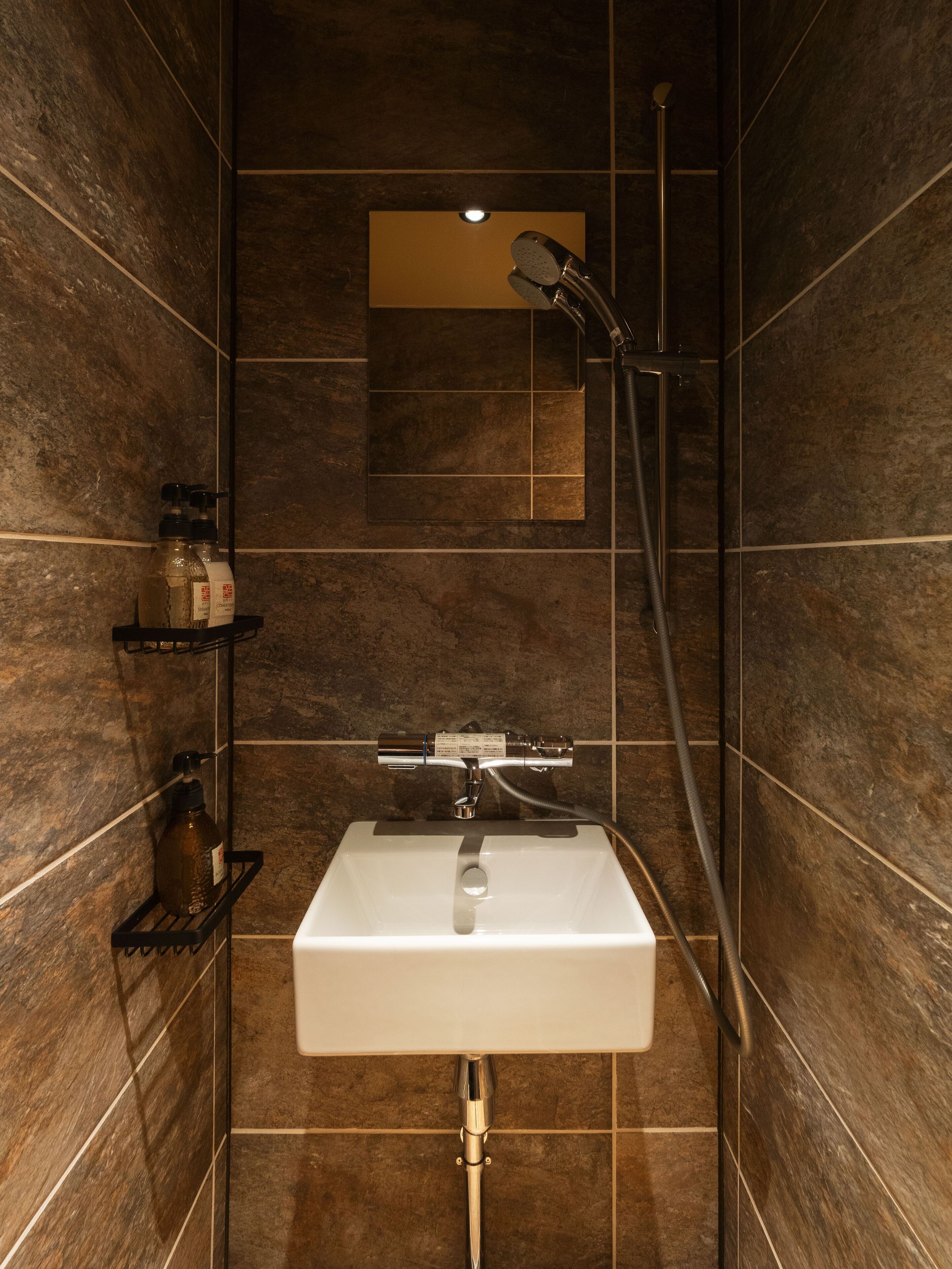 Een badkamer met een witte wastafel, een handdouche en een spiegel boven de wastafel.