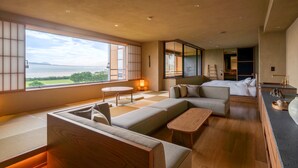 Een moderne hotelkamer met een groot raam met uitzicht op zee, een bank, een tafeltje en een bed.