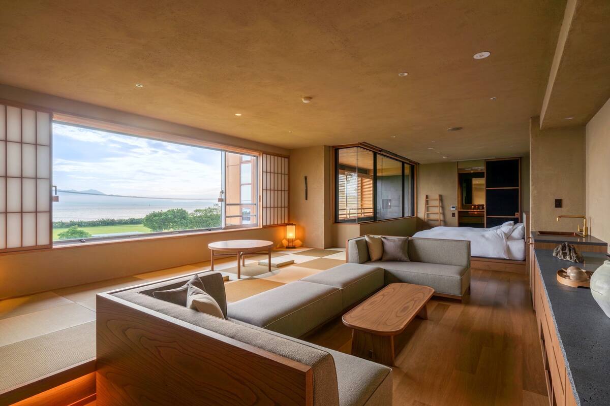 Een moderne hotelkamer met een groot raam met uitzicht op zee, een bank, een tafeltje en een bed.