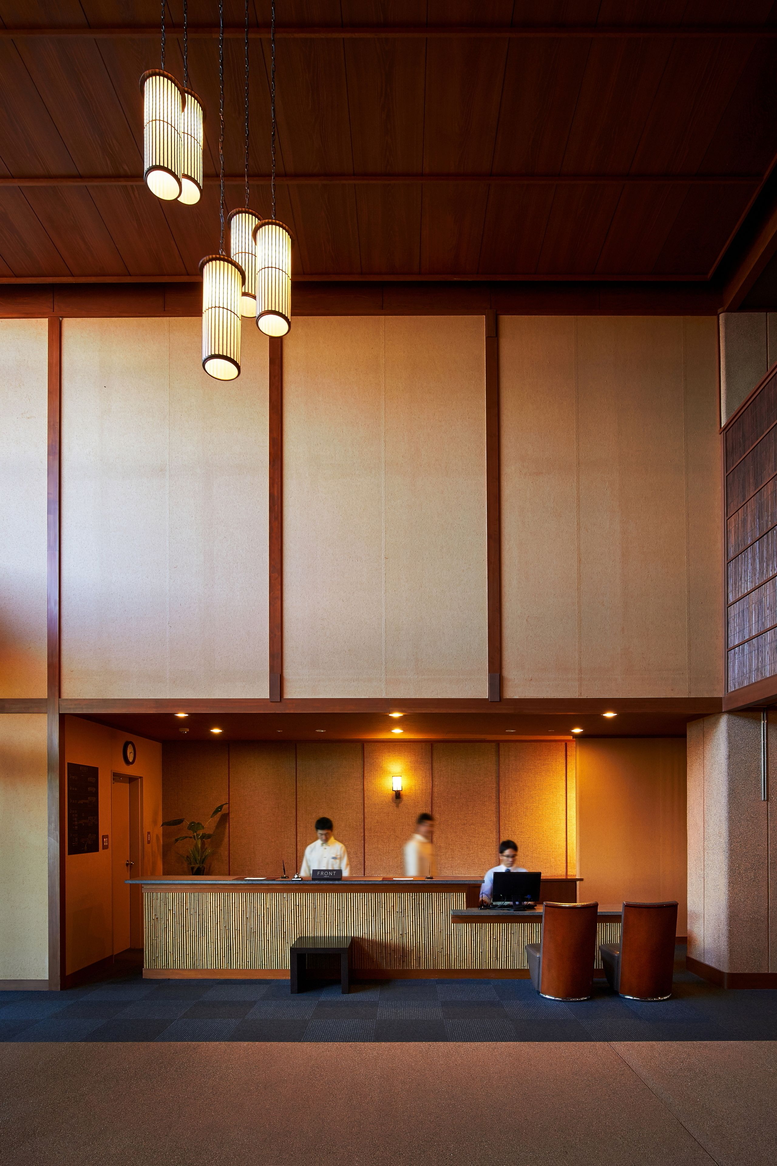 A reception area with a wooden reception desk, two seating areas, and hanging pendant lights.