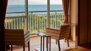 Een kamer met een balkon en uitzicht op zee, met een tafel, stoelen en een zeegezicht.