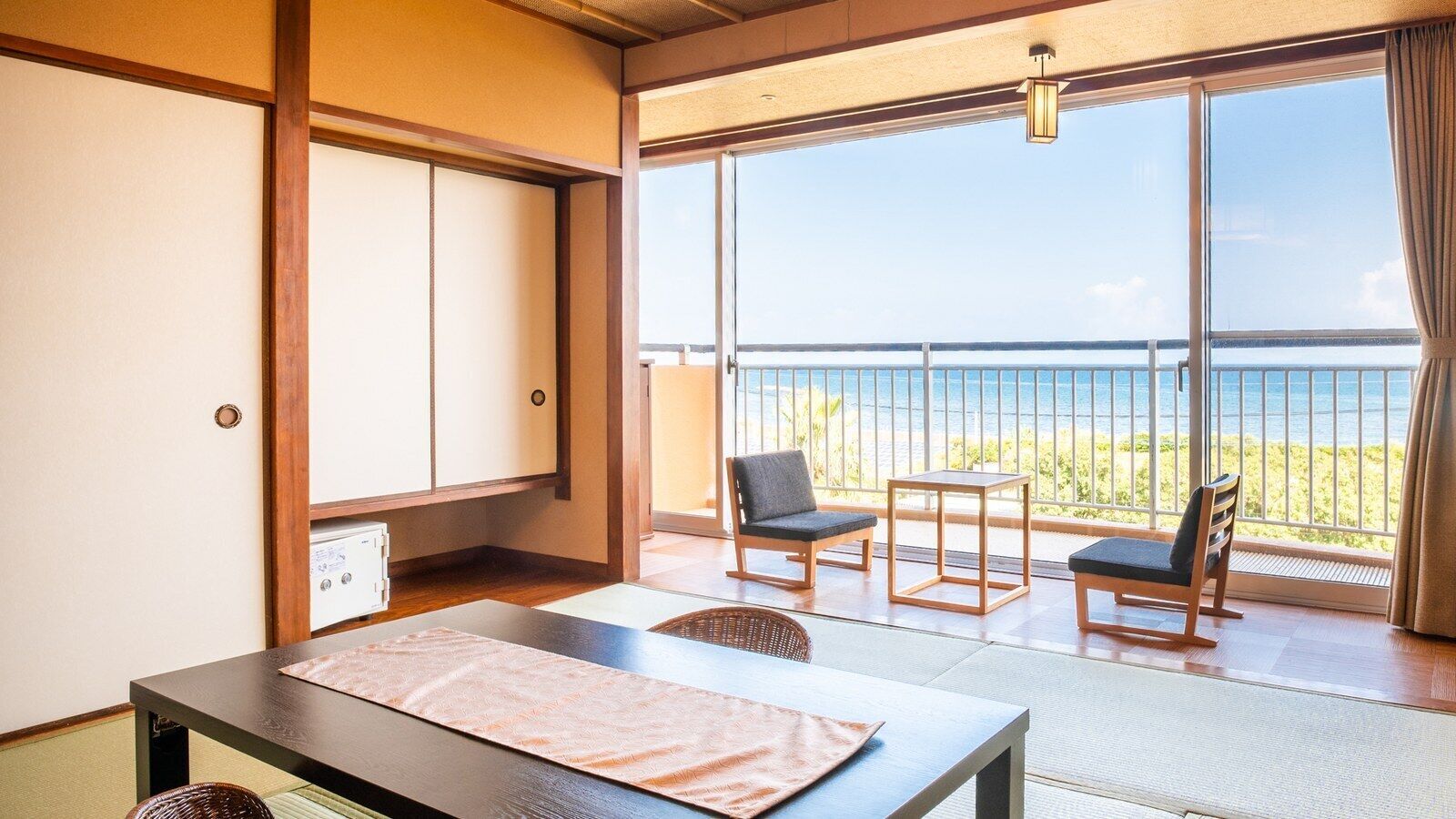 Una habitación con esteras de tatami, una mesa, sillas, una puerta corredera y un balcón con vistas al mar.