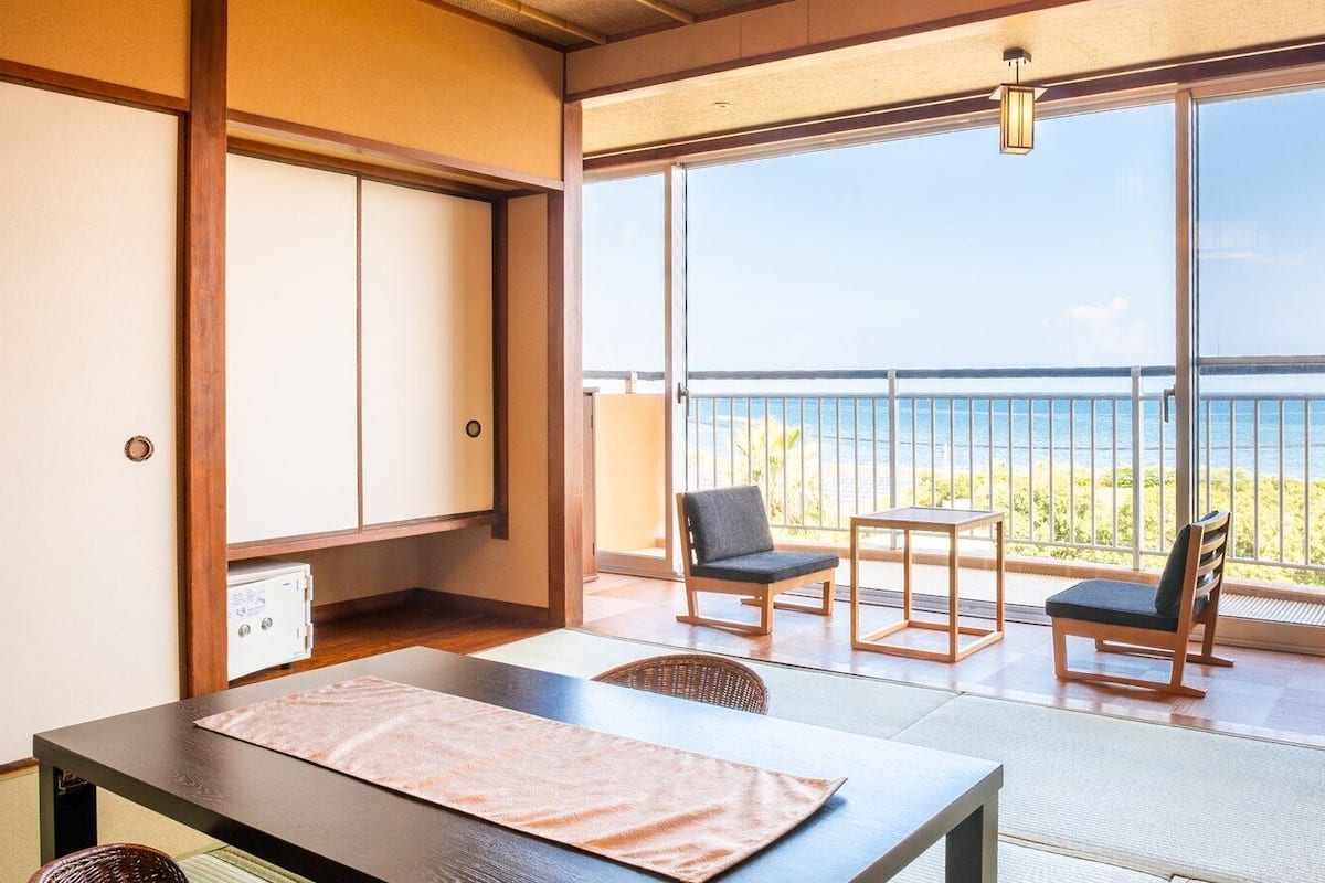 Una habitación con esteras de tatami, una mesa, sillas, una puerta corredera y un balcón con vistas al mar.