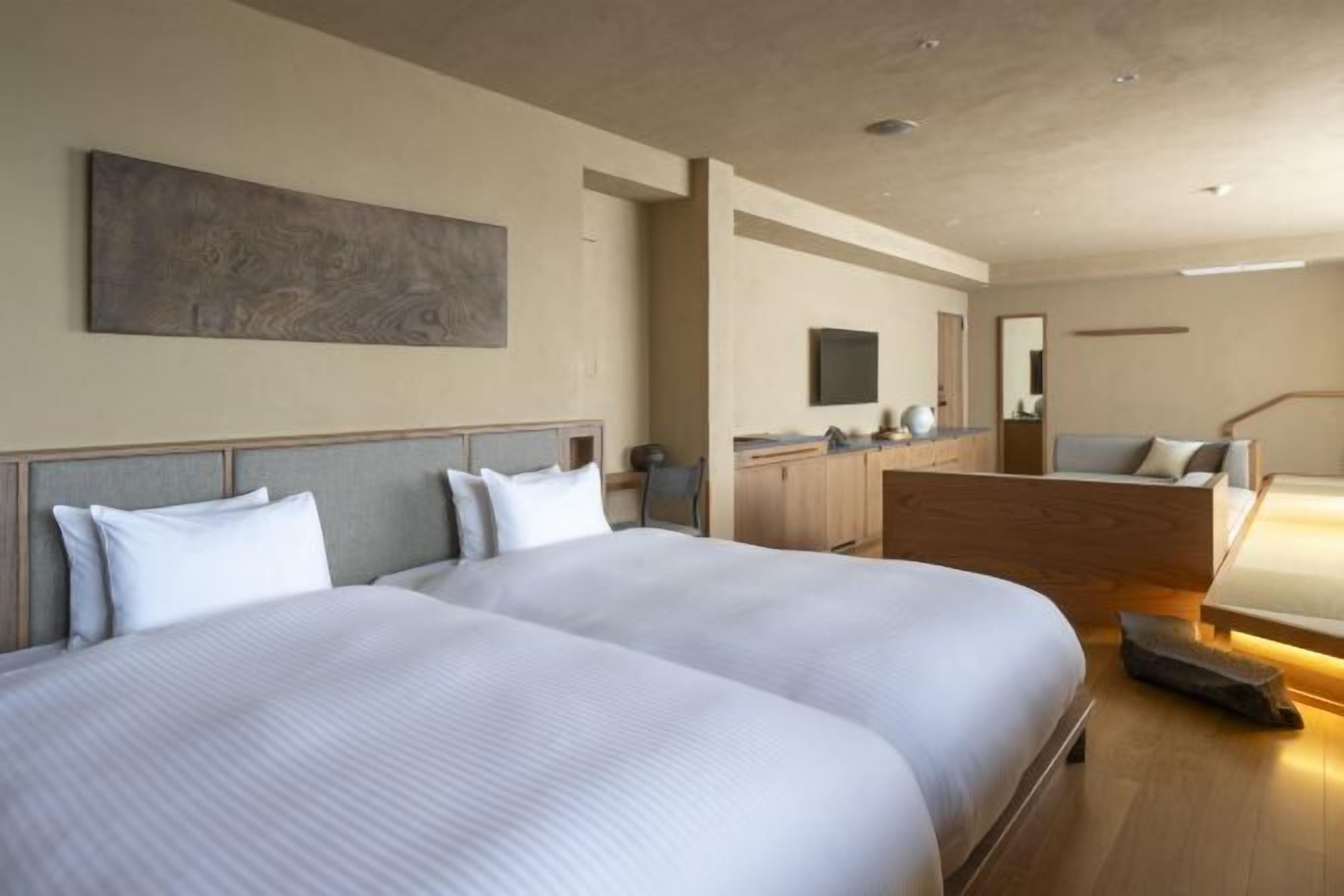 Ett hotellrum med två stora sängar, ett skrivbord, en stol och en TV.