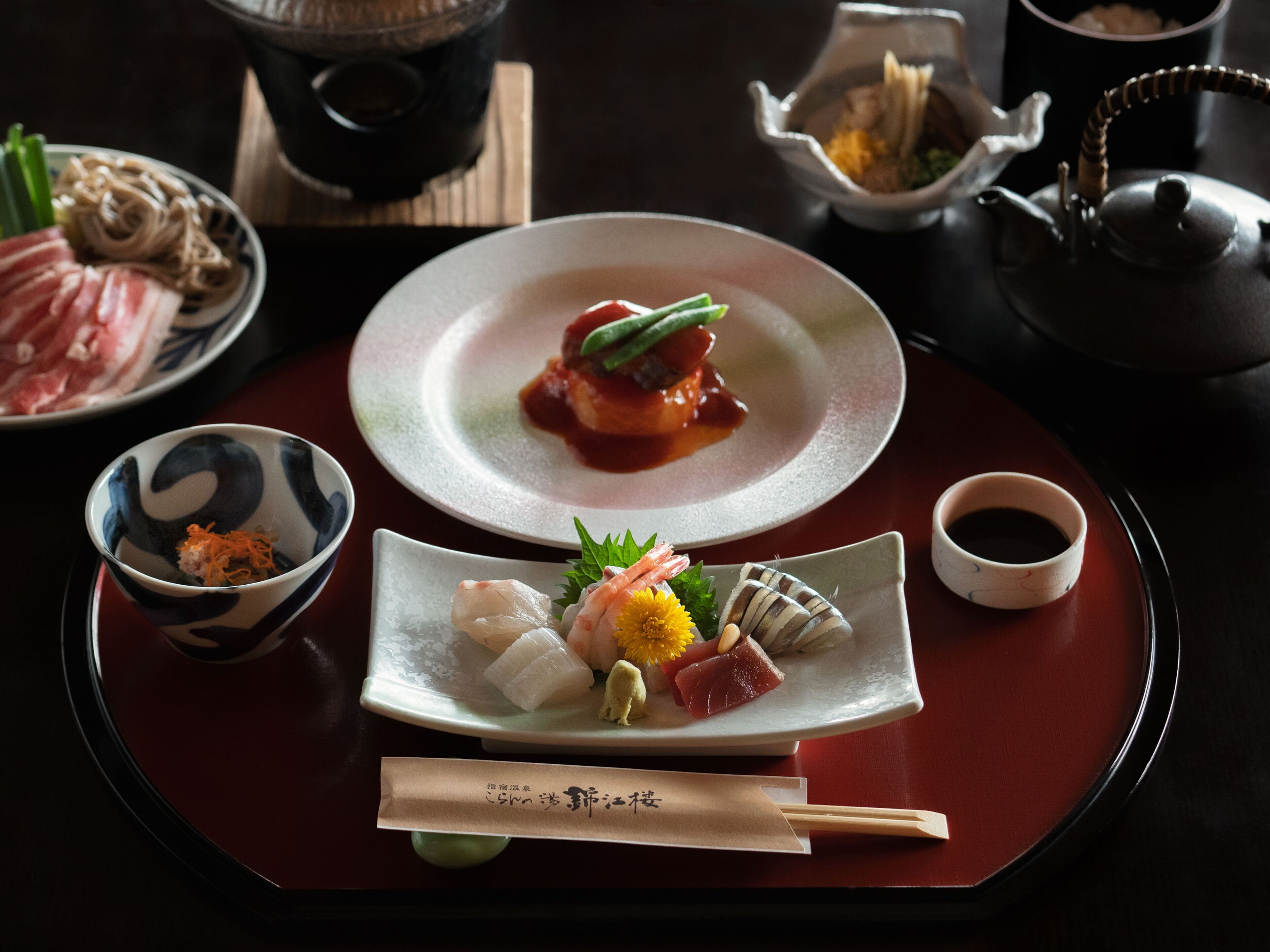 A traditional Japanese meal with various dishes on a tray, including sashimi and sushi, accompanied by small bowls of condiments and a teapot.