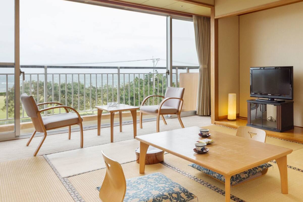 Een ruime kamer met balkon, een eettafel met stoelen, een televisie en een traditionele Japanse tatami vloer.