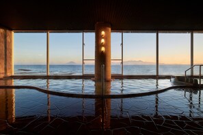 A large indoor pool with a view of the sea and mountains, a central column with lights, and a tiled floor. - Koran no Yu Kinkouroh (Ibusuki)