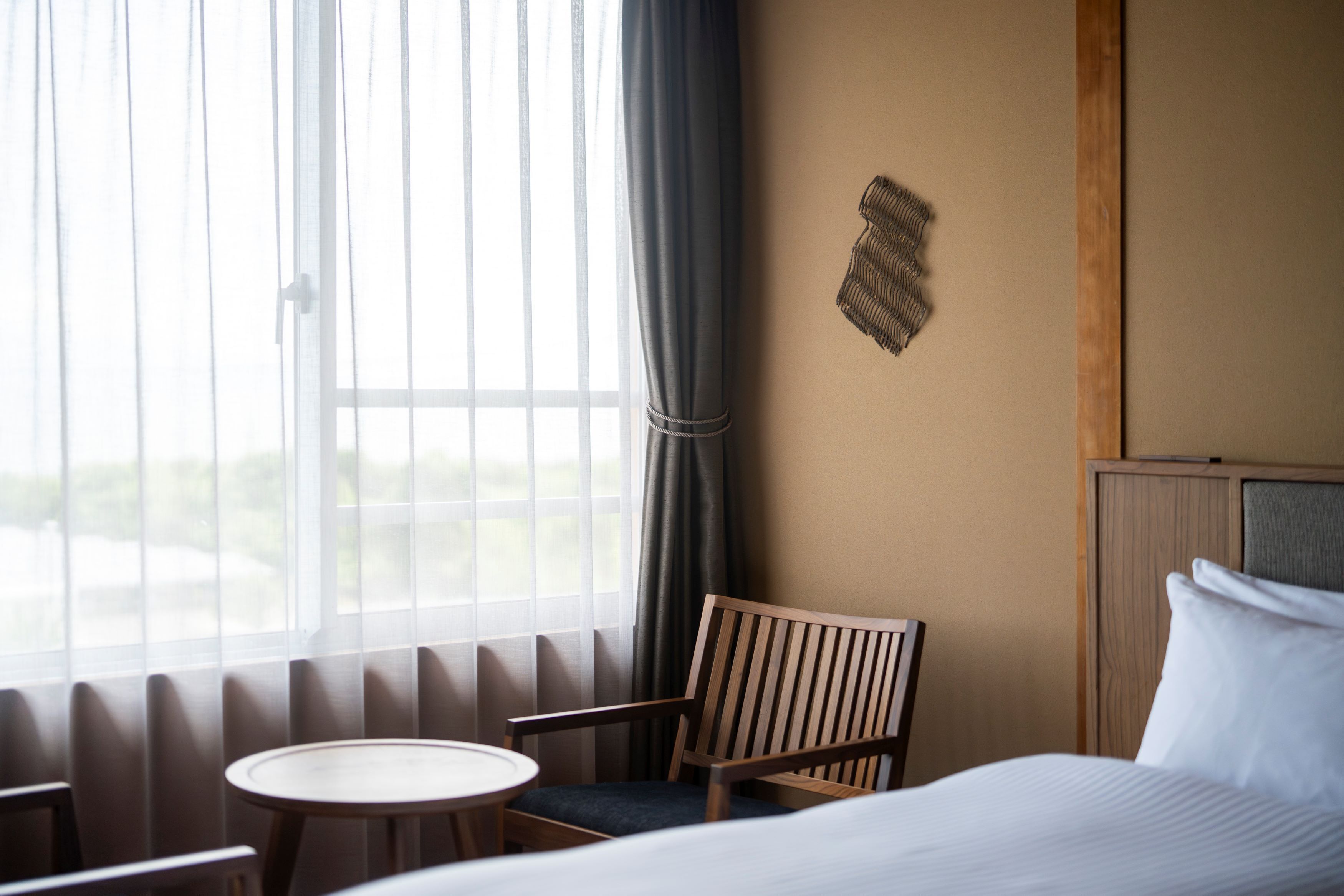 Habitación de hotel con cama, una mesita redonda, una silla de madera y una ventana con cortinas.