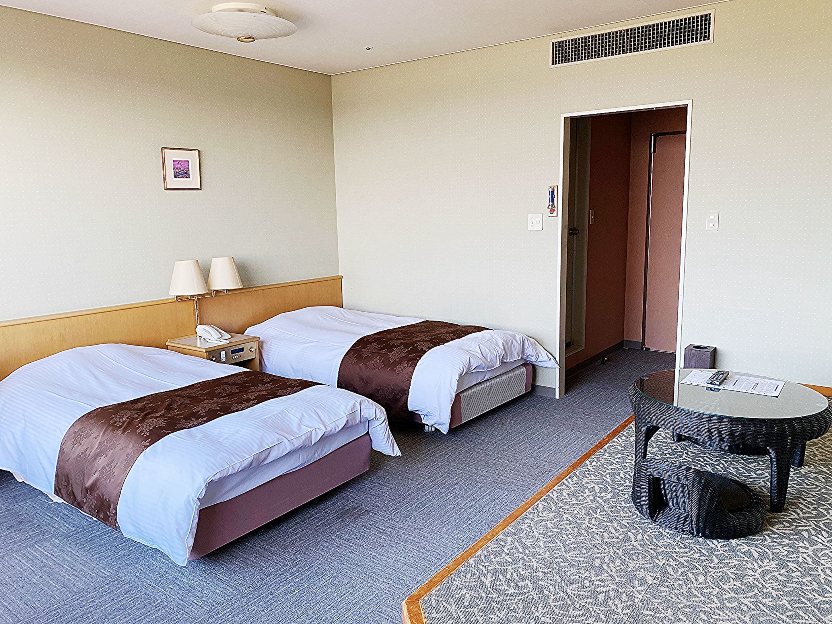 Habitación de hotel con dos camas, una mesita, una lámpara y un cuadro en la pared.