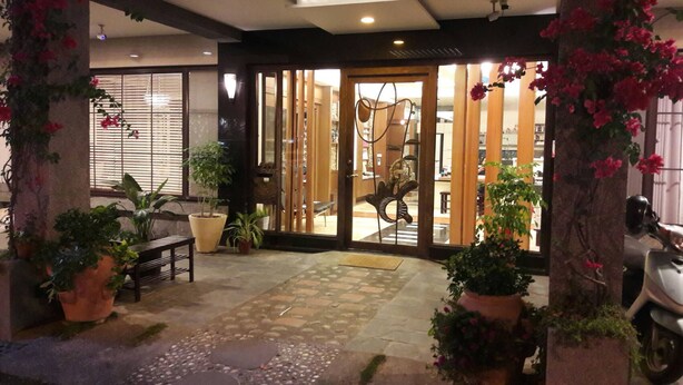 A hotel entrance with a tiled patio, potted plants, and a scooter parked outside.