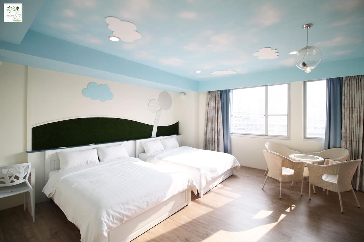 A hotel room with two beds, a round table with chairs, a desk, and a large window with curtains.