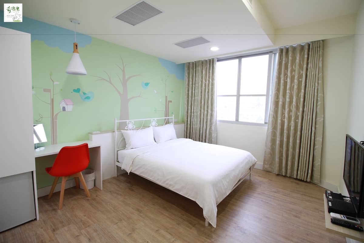 A bedroom with a bed, a desk with a chair, a television, and a window with curtains.