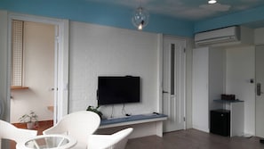 A living room with a flat-screen TV mounted on a white brick wall, a ceiling light, and a small table with a plant. - Key We Go (Tainan)