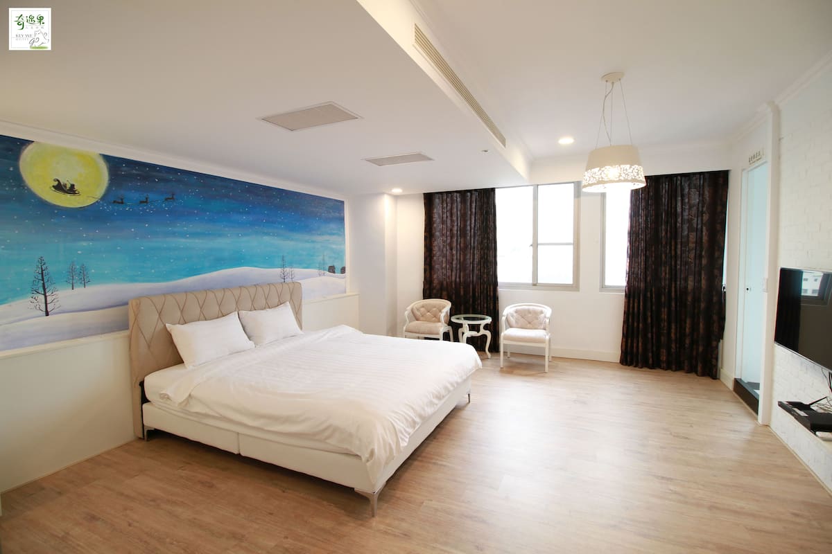 A bedroom with a large bed, a night sky mural, two chairs, a TV, and a window with curtains.